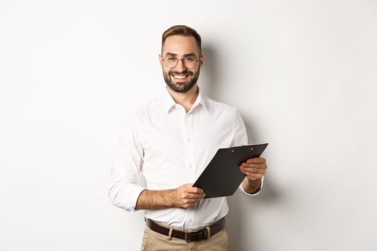 Handsome manager in glasses working, using clipboard, standing over white background.
